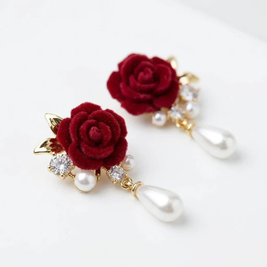 A pair of gold-tone drop earrings featuring deep red velvet roses, small clear crystal accents, and white pearl teardrop drops, displayed on a clean white background.