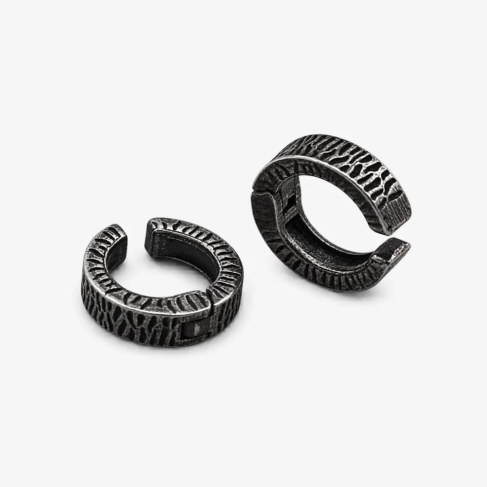 A pair of textured black metal huggie hoop earrings with a hammered finish, displayed in side view.