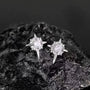 Star-shaped silver earrings with clear stones on a dark rock background