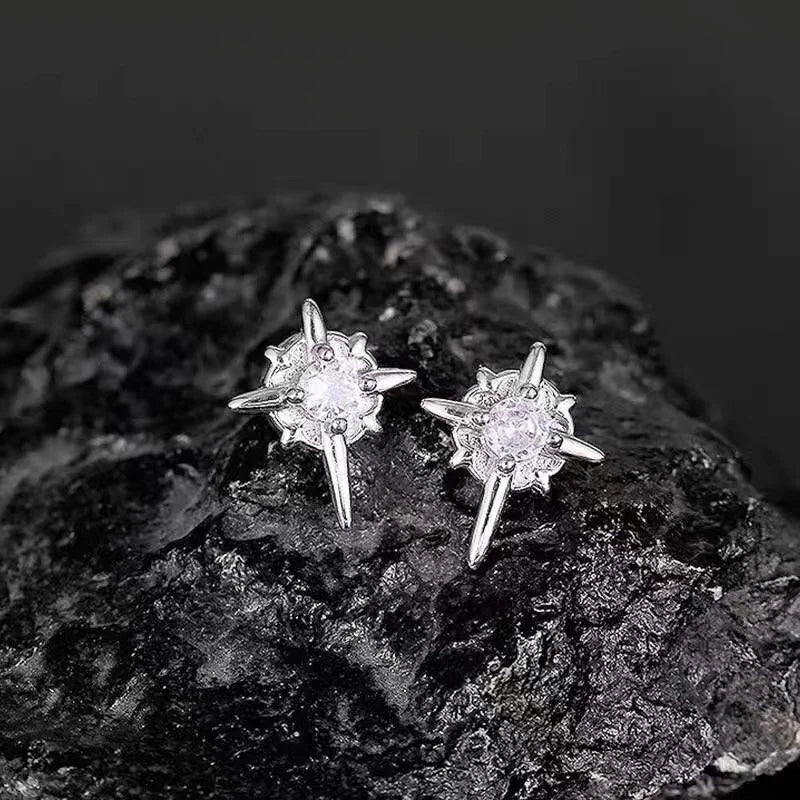 Star-shaped silver earrings with clear stones on a dark rock background