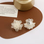 White flower clip on earrings displayed on brown leather pad with silver hardware detail visible