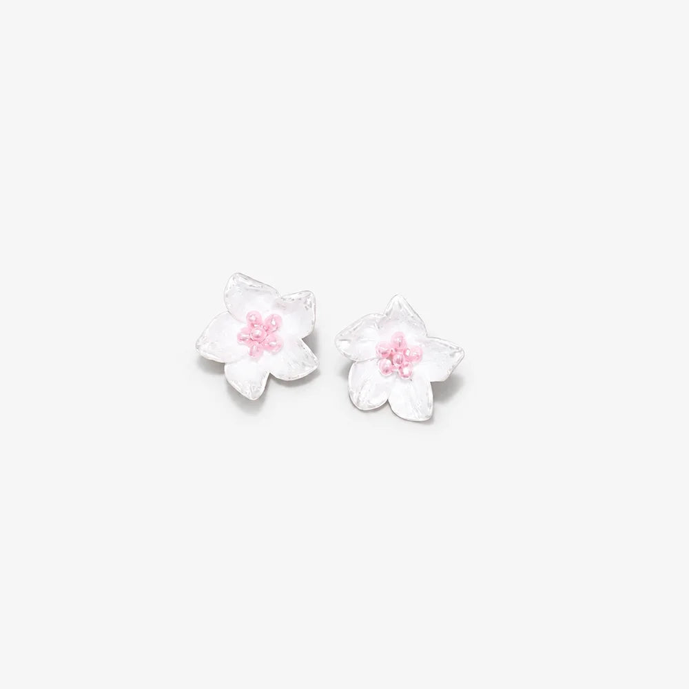 A pair of white cherry blossom stud earrings with textured petals and small pink centers, shown on a plain light gray background.