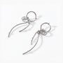 A pair of silver-toned dangle earrings with curved leaf-like wire branches and small clear stones, displayed on a clean white background.

