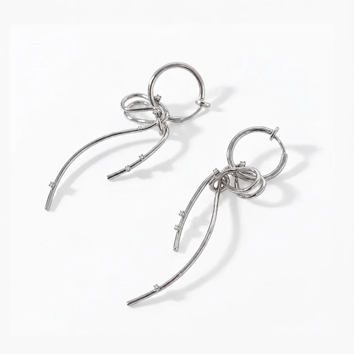 A pair of silver-toned dangle earrings with curved leaf-like wire branches and small clear stones, displayed on a clean white background.

