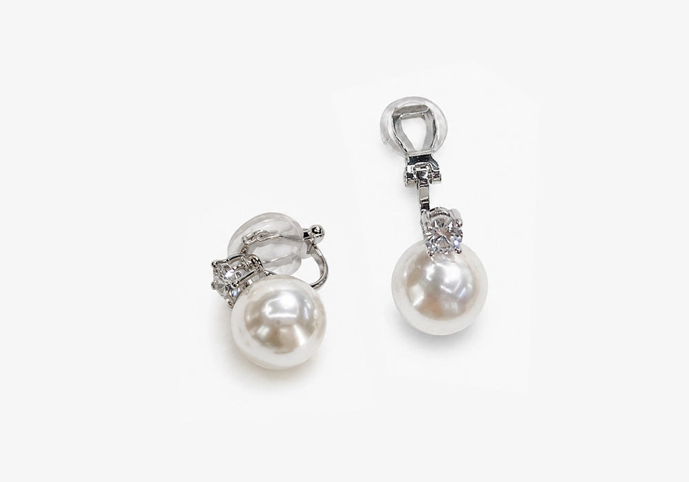 White pearl drop clip on earrings in silver, top view on white background displaying lustrous pearls and rhinestone accents