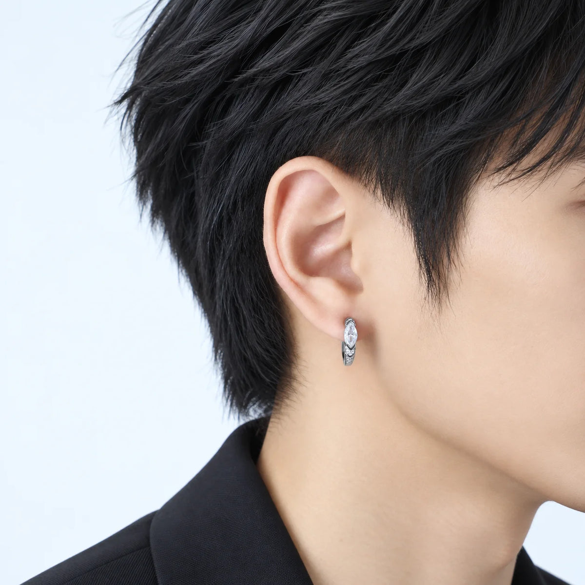 A close-up of a person's ear wearing a small silver earring with a white zircon design.