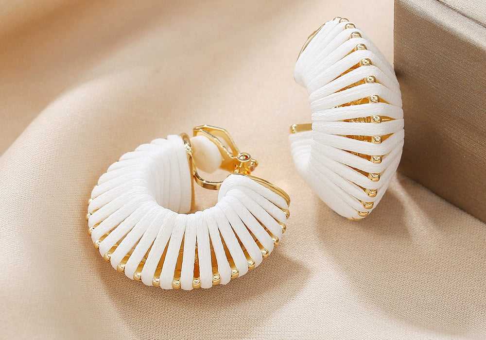 White leather wrapped clip-on hoop earrings displayed on beige fabric, showcasing gold accents and textured design detail