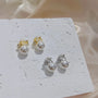 White pearl drop clip on earrings in gold and silver displayed on white textured surface with natural lighting