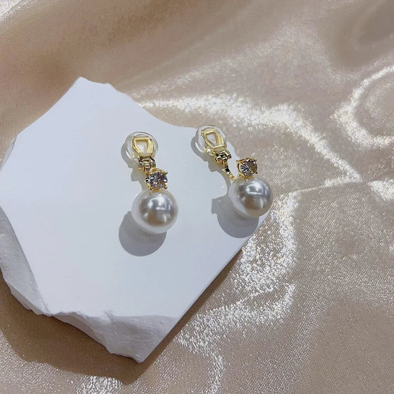 White pearl drop clip on earrings in gold displayed on white ceramic stand with gold hardware and rhinestone accents