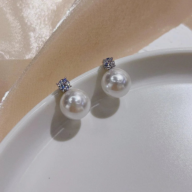 White pearl drop clip on earrings in silver displayed on white ceramic dish with beige fabric background