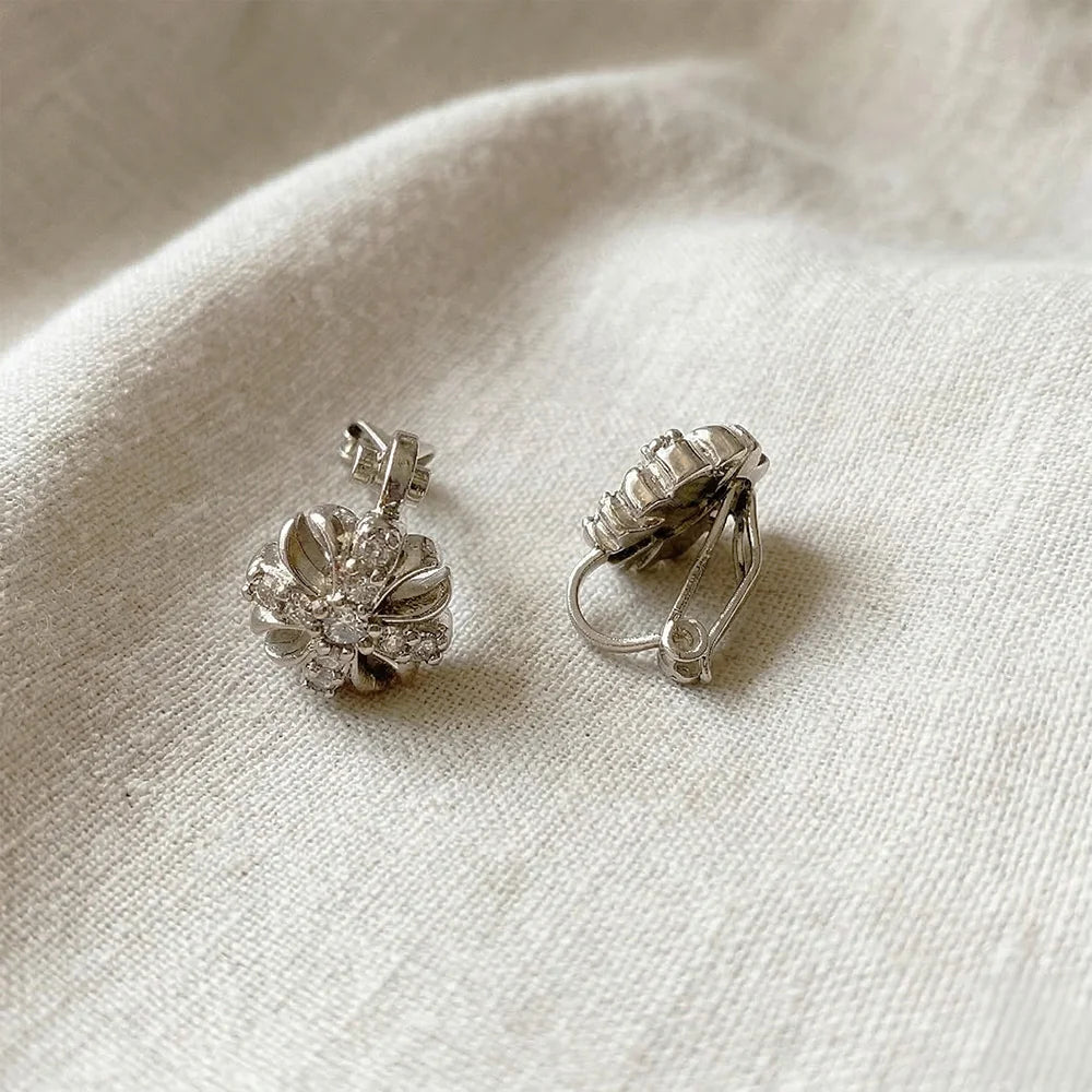 White gold cross clip-on stud earrings displayed on cream fabric, showing detailed front view of textured metal design