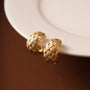 Gold woven crescent clip-on hoop earrings displayed on white plate with brown background