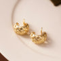 Gold woven crescent clip-on hoop earrings displayed on white ceramic dish, front angle view