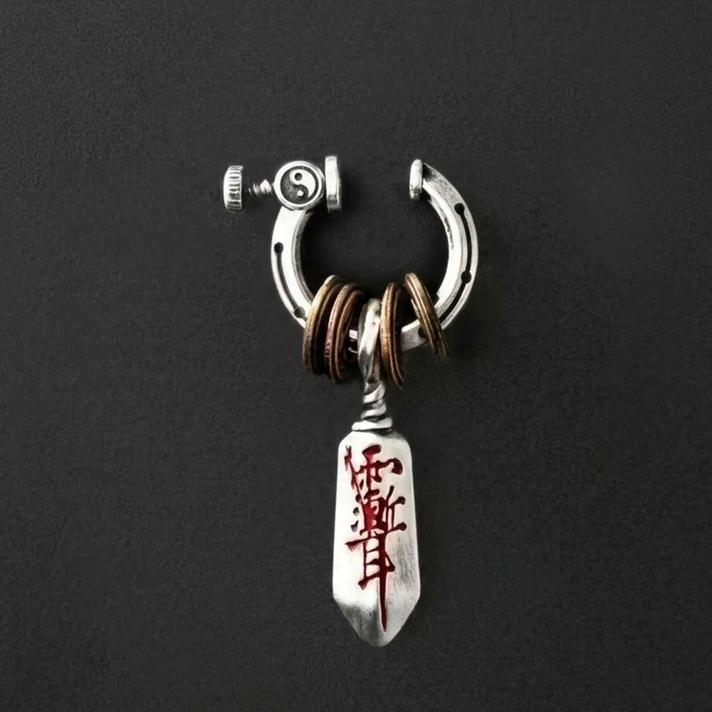 A focused product shot of the Katana dagger clip-on single earring on a textured dark black background. The red Japanese calligraphy and aged metal textures are highly visible.