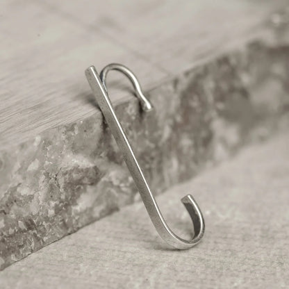 The Axis minimalist sterling silver ear cuff displayed leaning against a piece of grey stone, highlighting its shape.