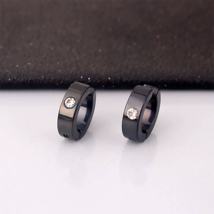 A pair of black minimalist clip-on huggie hoops with a single zircon stone, displayed on a white surface against a dark background.