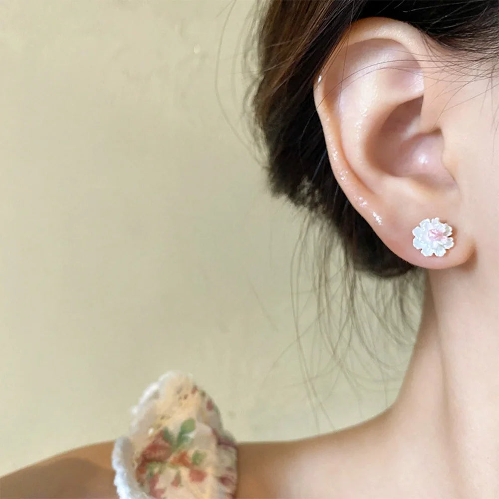 A model wearing one white cluster petal magnetic stud earring with a pink center, showcasing the earring comfortably on an ear.