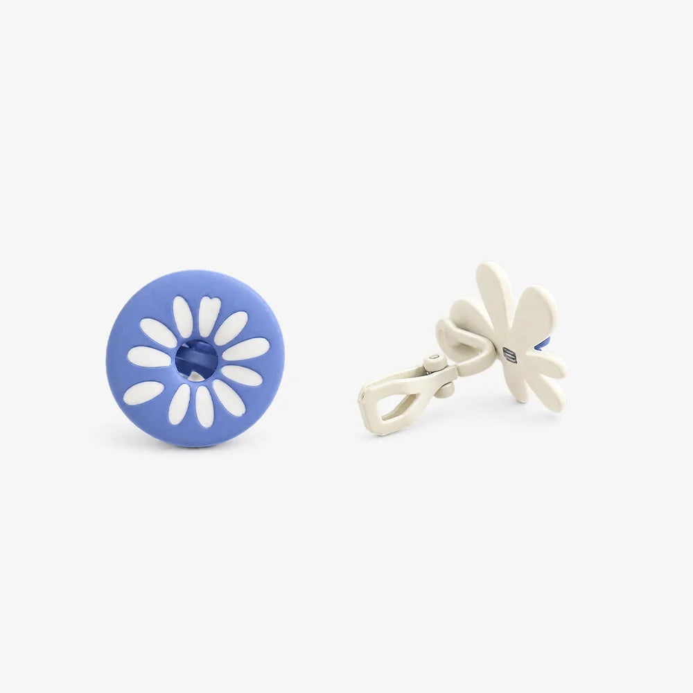 A pair of flower-shaped clip on earrings on a light gray background. One cufflink is shown from the front, featuring a blue circular face with a white daisy pattern and a blue center.