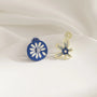 Blue flower mismatched clip-on earrings displayed on white fabric background, showing blue and cream daisy designs