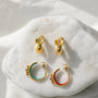 A collection of gold bohemian cross motif clip on hoops with turquoise and crimson enamel linings displayed in a lifestyle setting.