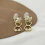 Bow-Tied Bear Pearl Clip-On Earrings in gold and white displayed on tan plate angled view