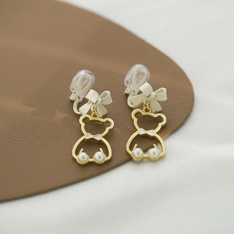Bow-Tied Bear Pearl Clip-On Earrings in gold and white displayed on tan plate angled view