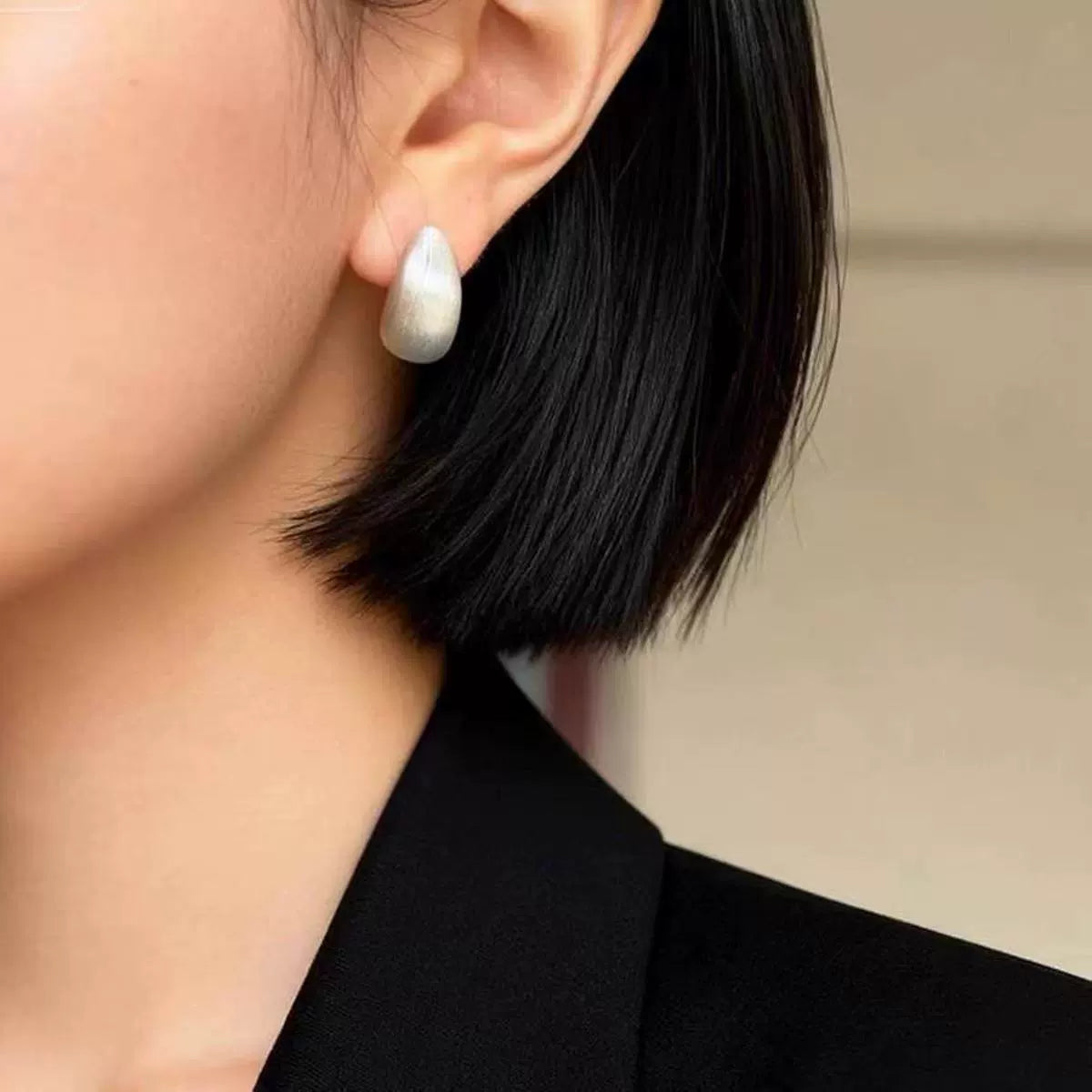 Brushed dome clip-on earring worn on a non-pierced earlobe with a black blazer