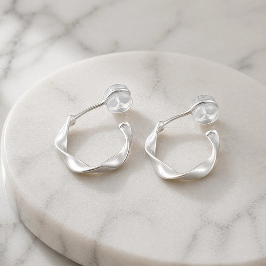 Close-up of brushed silver sculptural clip-on earrings on a marble surface showing the comfort c-type clip on.