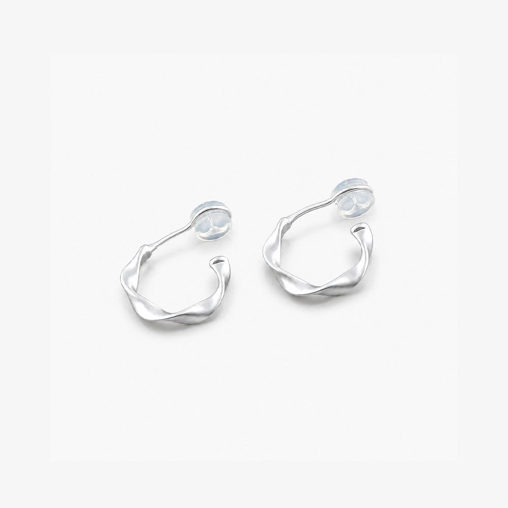 Close-up of brushed silver sculptural clip-on earrings on a marble surface showing the comfort c-type clip on.