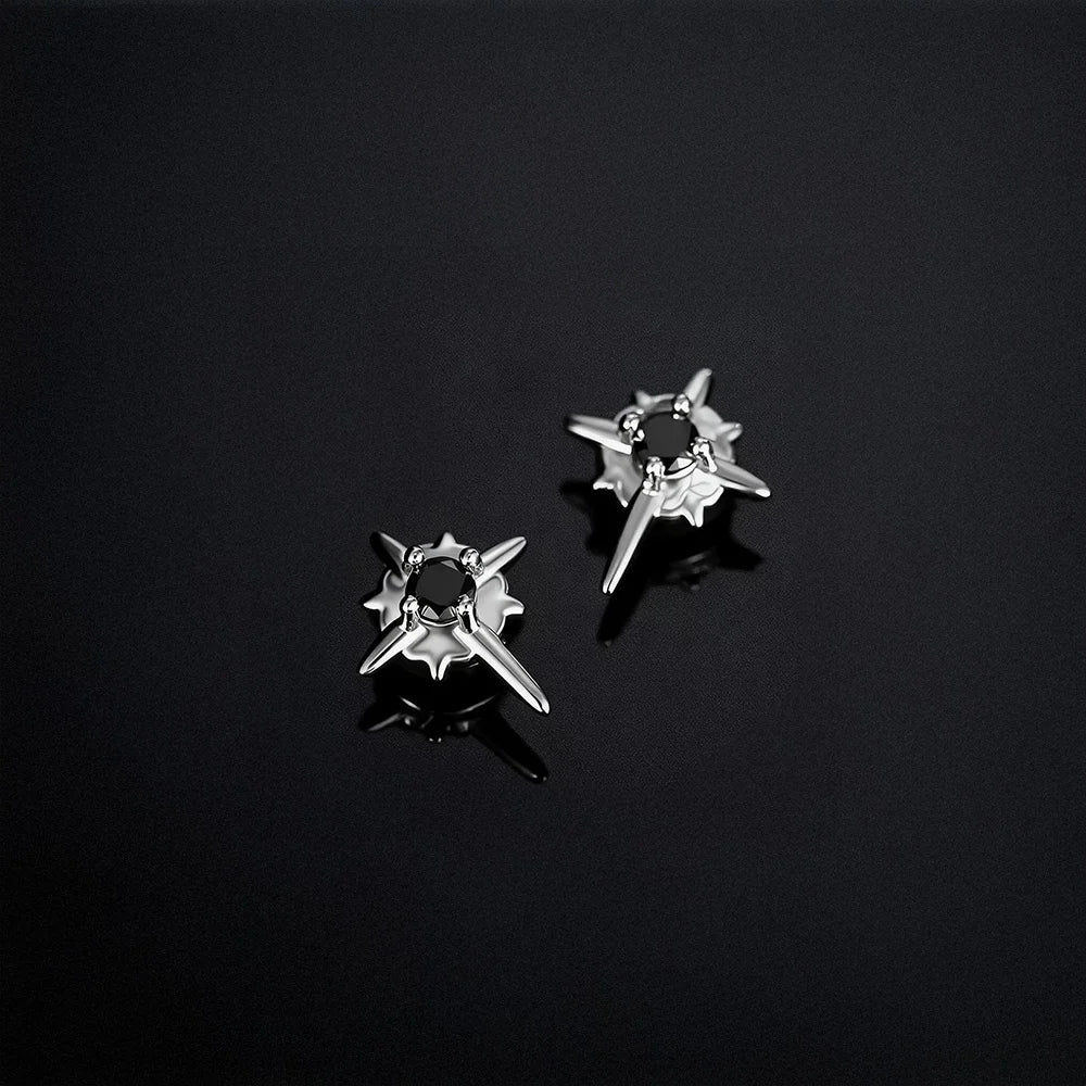 A pair of celestial black star magnetic stud earrings displayed on a reflective dark surface, highlighting their edgy design.