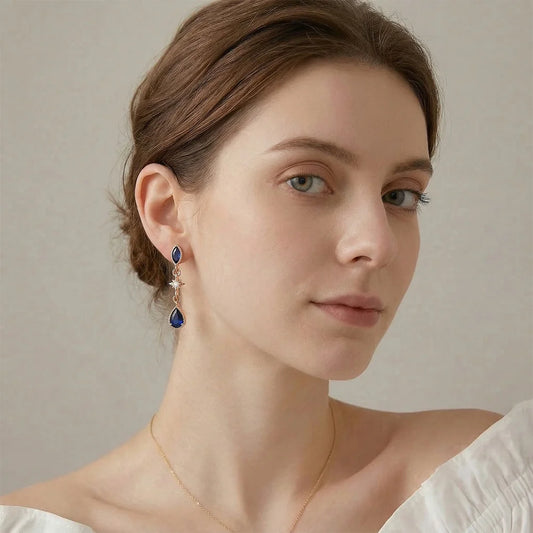 A fashion model wearing the Midnight Star sapphire drop earrings with a sleek updo, demonstrating the elegant hang and scale of the celestial jewelry.