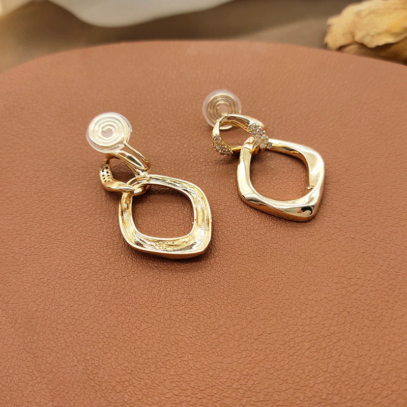 A close-up view highlighting the intricate pavé zircon details on the connector link of the gold geometric clip-on earrings.