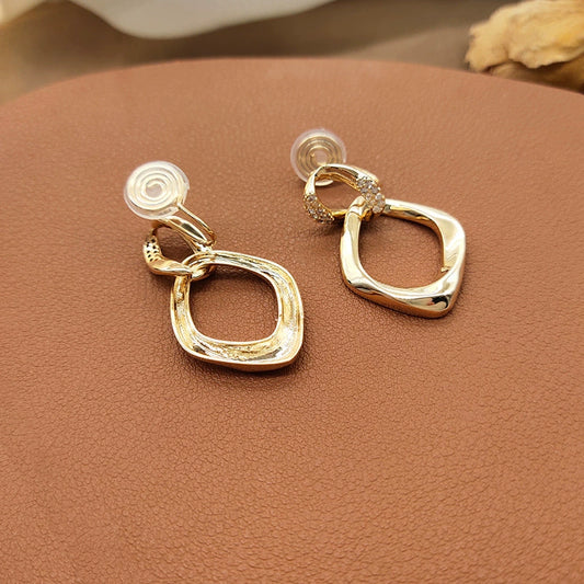 A close-up view highlighting the intricate pavé zircon details on the connector link of the gold geometric clip-on earrings.