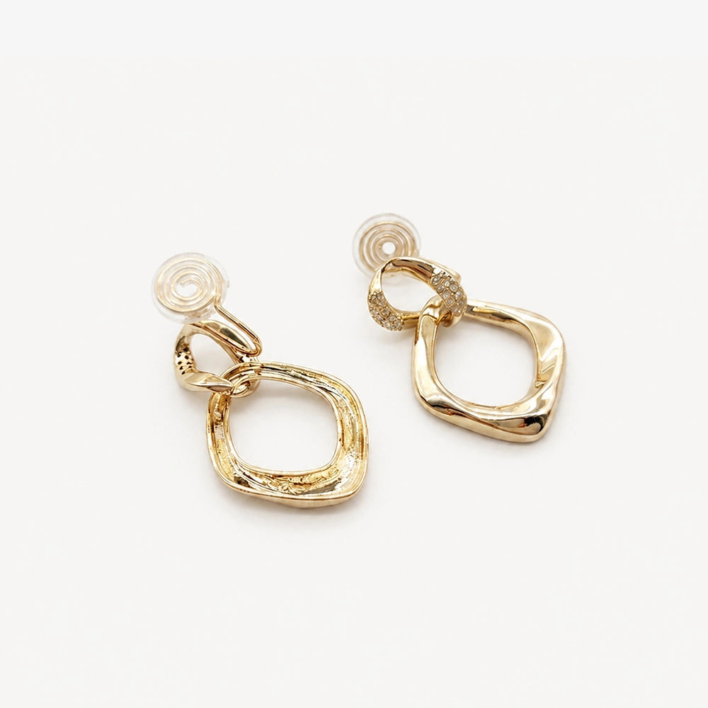 A close-up view highlighting the intricate pavé zircon details on the connector link of the gold geometric clip-on earrings.
