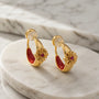 Close-up of crimson enamel and gold bohemian ear clips on a natural stone surface highlighting the cross design and CZ sparkle.