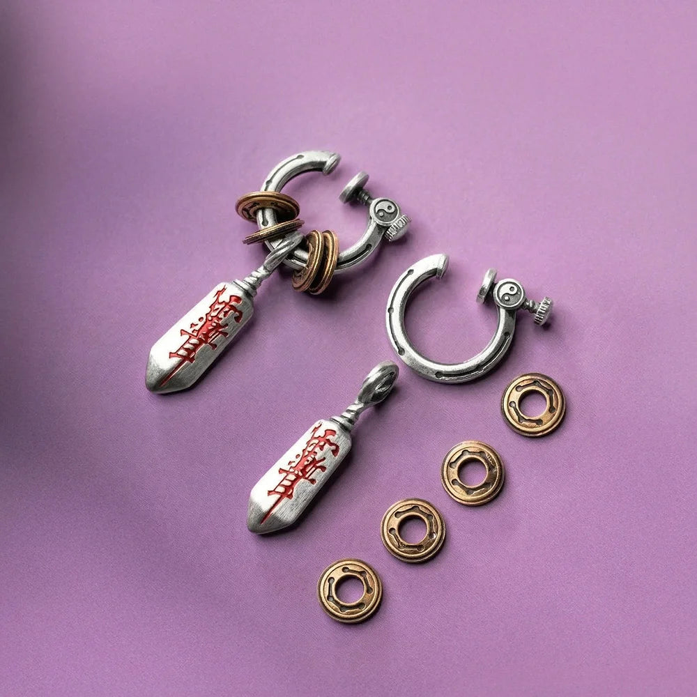A flat lay composition on a purple background showing two dagger pendants, a separate silver clip-on hoop, and a row of four loose bronze coin spacers, highlighting the individual parts of the earring design.