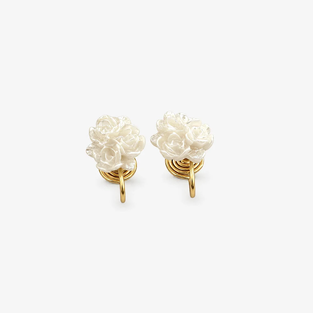 A pair of white resin flower clip-on earrings with comfortable mosquito coil clips displayed on a white surface next to a satin cloth.