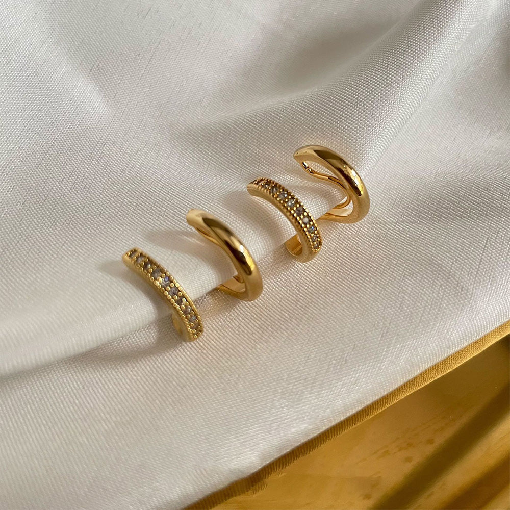 Gold-toned double hoop clip-on earrings adorned with sparkling zircon inlays present a bold statement. Their contemporary design exudes modern elegance, crafted with a durable alloy and secured with a coil clip-on for ease of wear without the need for pierced ears. 