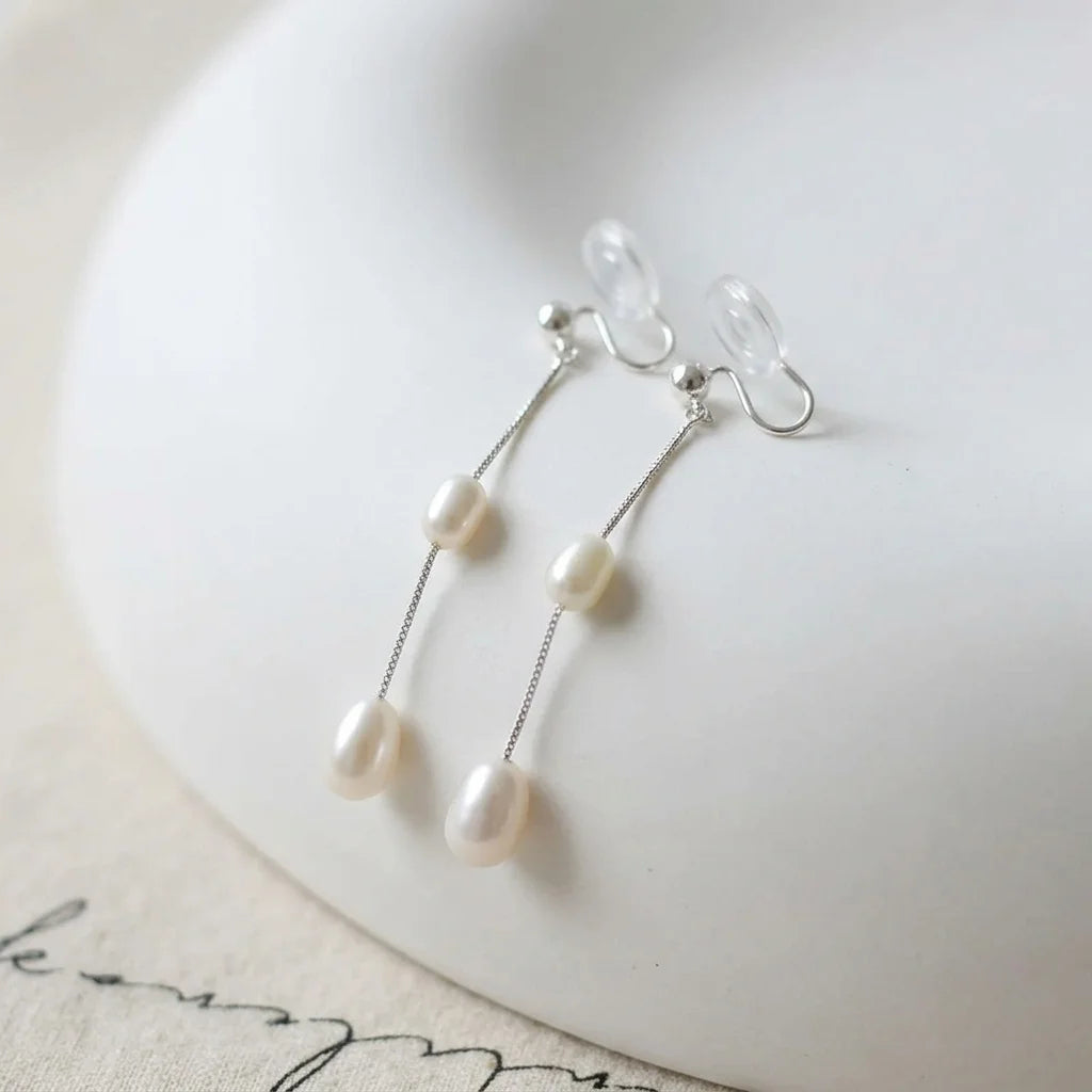Double freshwater pearl clip-on earrings with clear resin pads displayed on a white stand