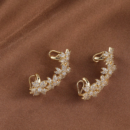 Detail of warm gold Blossom Flower Crystal Helix Ear Cuffs against a brown backdrop, the zircon gems twinkling amidst the petal shapes, reflecting a luxurious and nature-inspired bridal accessory.