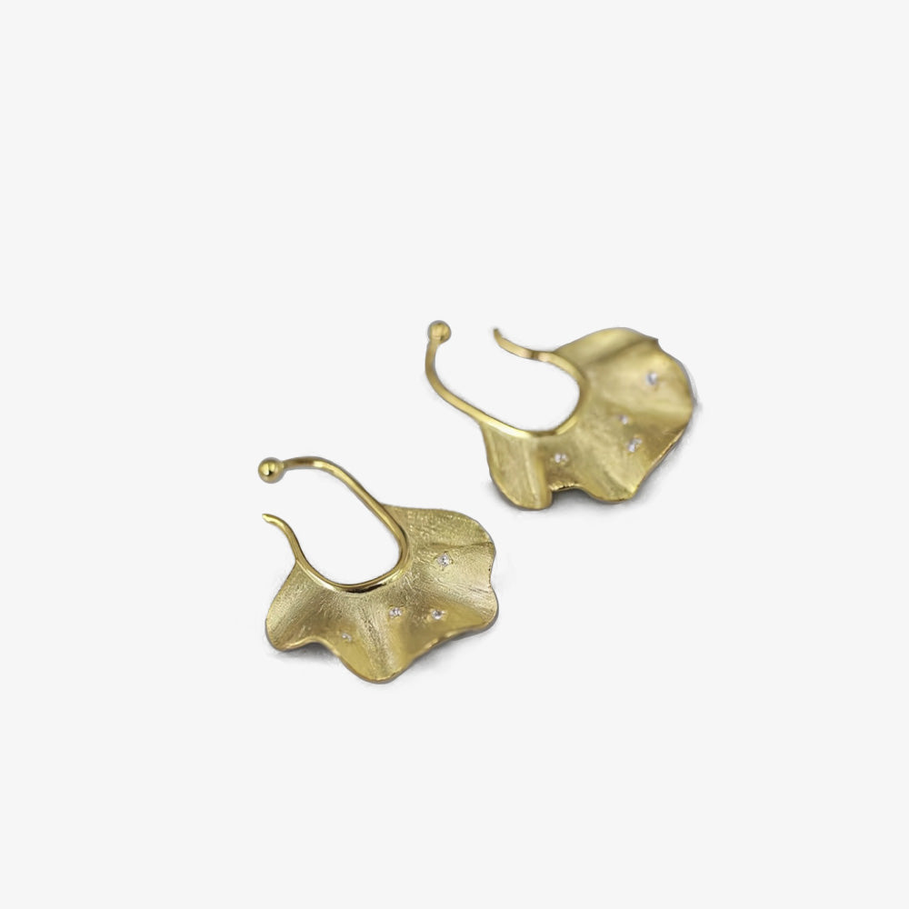 Gold Ginkgo Leaf Ear Cuff Earrings set on a white surface, featuring sparkling white zircon inlays that capture the light, reflecting the organic beauty and luxury of the conch cuff earrings.