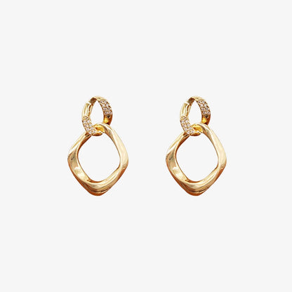 Pair of gold geometric pave drop earrings on a light gray background