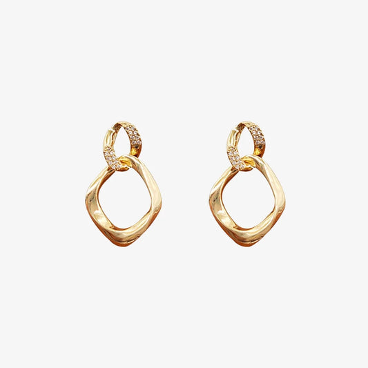 Pair of gold geometric pave drop earrings on a light gray background