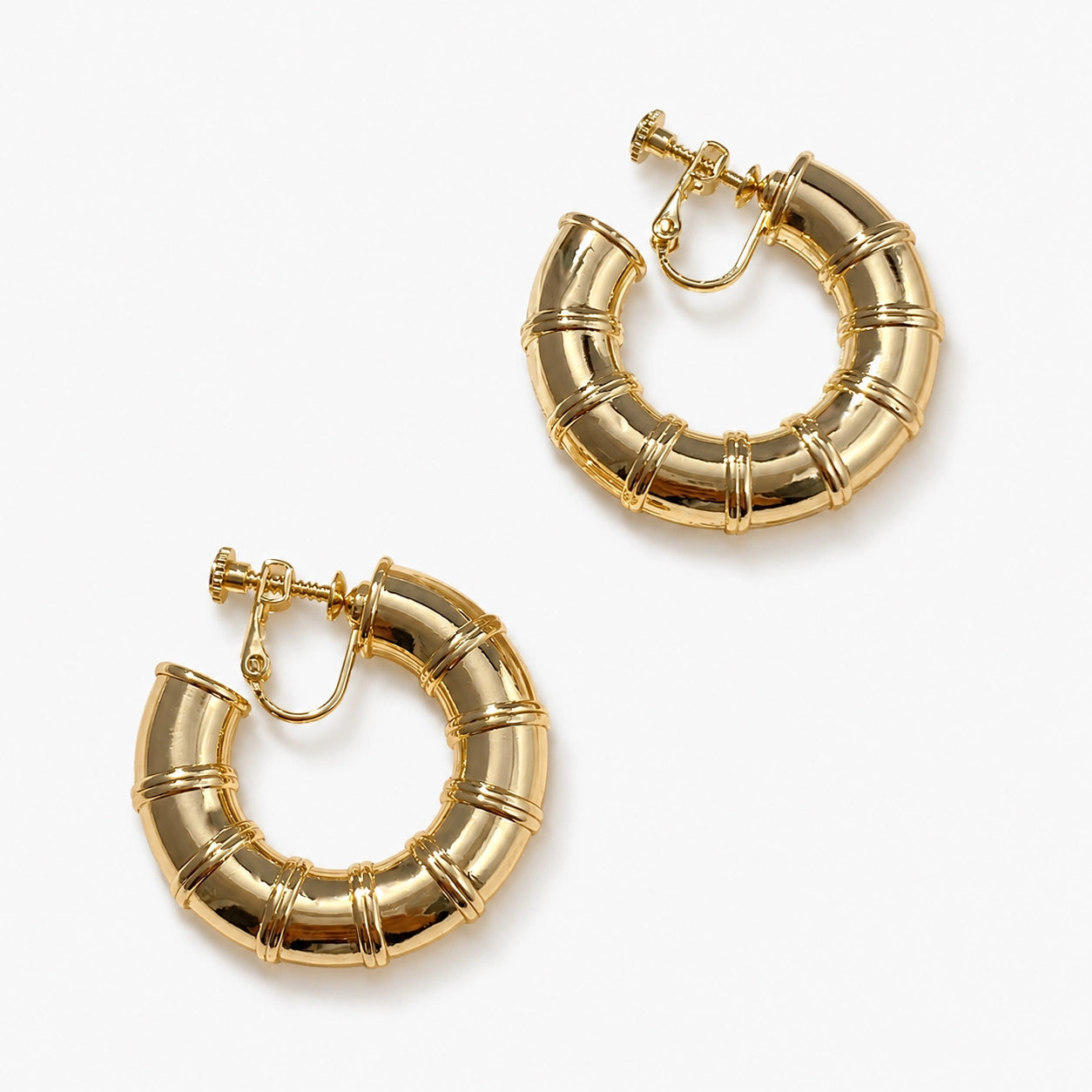 Gold bamboo hoop clip on earrings displayed on white ceramic dish and beige surface, top view