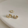 An artful display of the trio of gold and pavé zirconia ear cuffs on a neutral, curved white surface.