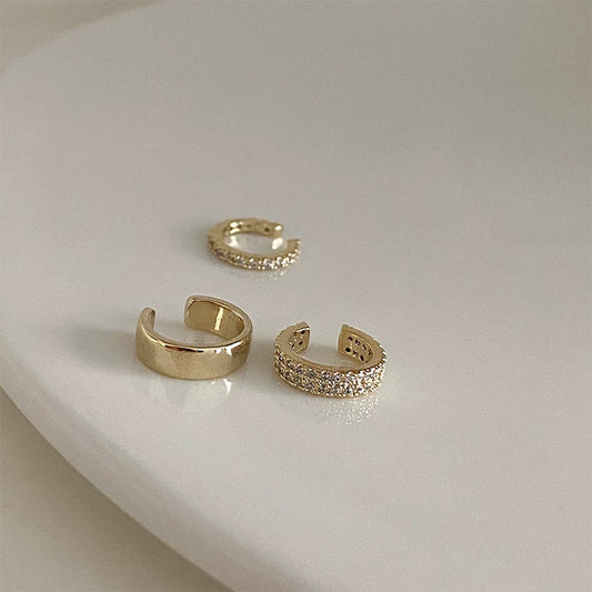 An artful display of the trio of gold and pavé zirconia ear cuffs on a neutral, curved white surface.
