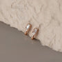 Rose gold earrings with clear gemstones on a textured stone surface