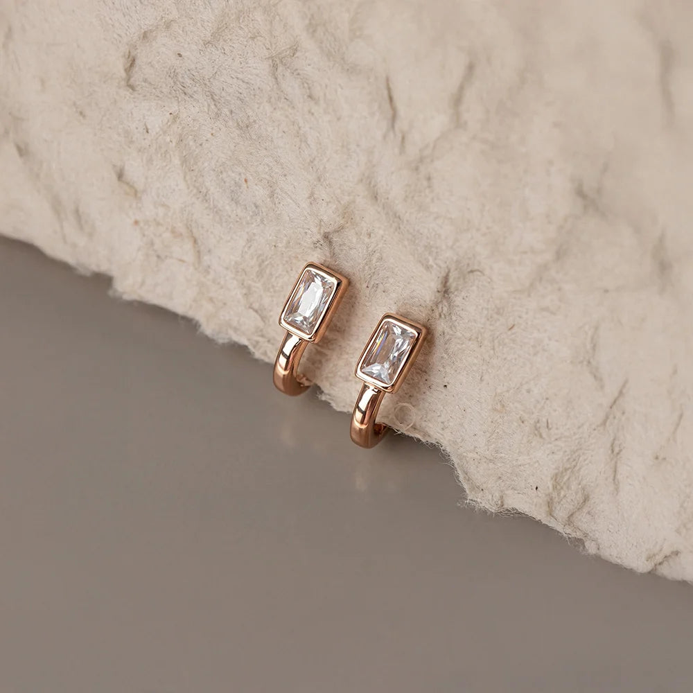 Rose gold earrings with clear gemstones on a textured stone surface