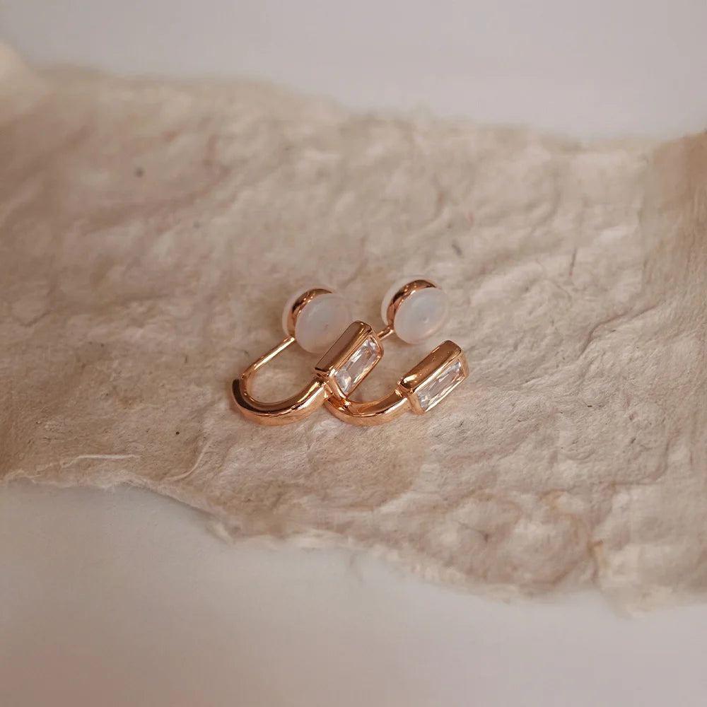 Rose gold earrings with clear stones on a textured beige surface
