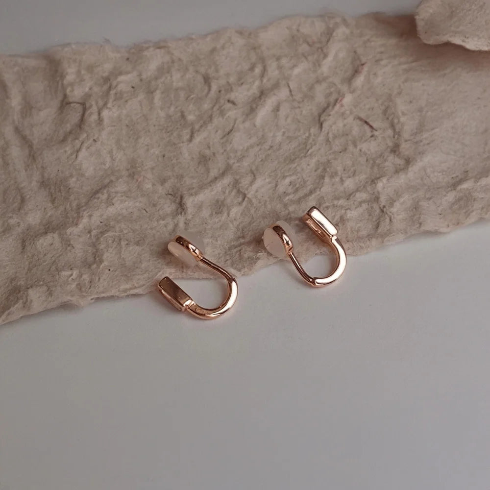 Rose gold earrings with comfortable clip on design on a textured beige surface